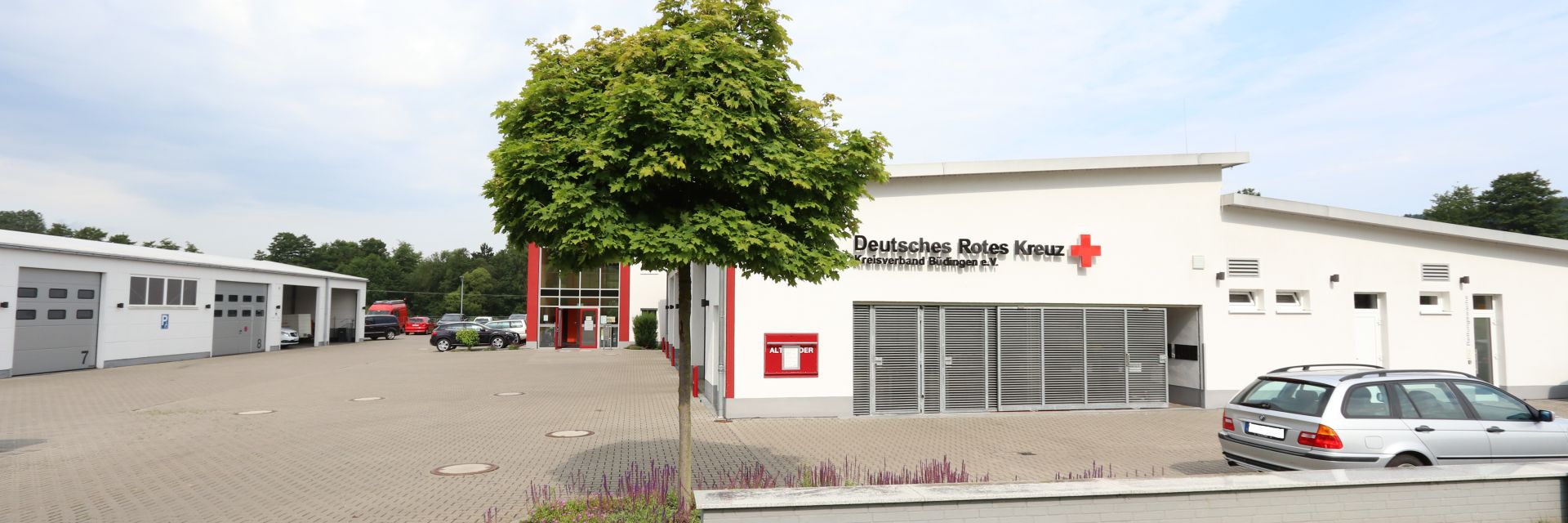 Foto: Zwei ältere Damen lehnen sich aus einem großen Fenster und blicken freudig den nahenden DRK-Mitarbeiter an.